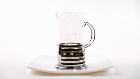 pouring hot water into a french press with tea leaves on a white plate, brewing process