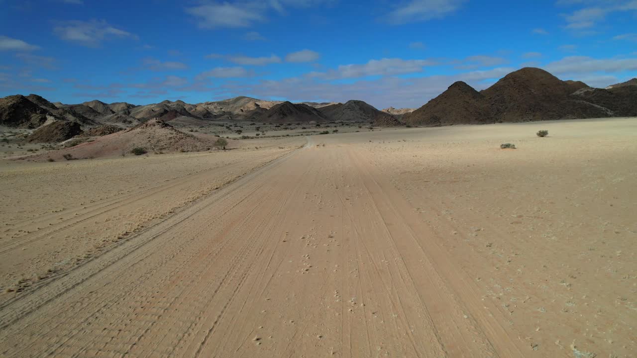 Aerial shot over a dry sandy desert road cutting through barren wilderness with distant mountains, evoking isolation, adventure, and the feeling of being lost