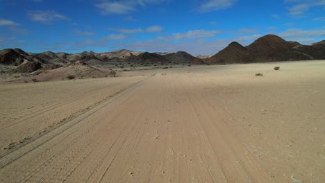 aerial shot over a dry sandy desert road cutting through barren wilderness with distant mountains, evoking isolation, adventure, and the feeling of being lost