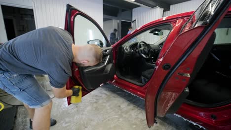 man worker washing red car on a car wash with yellow washcloth.