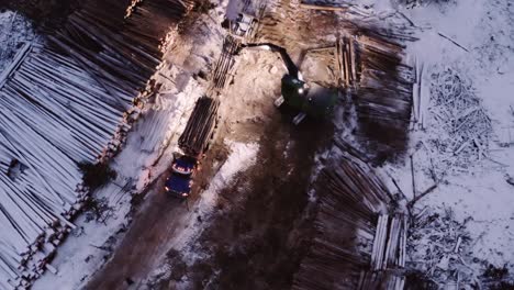 aerial top down drone cranes down as timber manipulator fills up timber transportation truck from nearby snow covered cut down mature pine trees piles