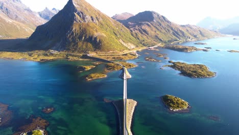 Drone-flying-over-lonely-road-bridge-towards-an-iconic-and-steep-mountain-in-northern-Norway-surrounded-by-the-sea-and-many-small-islands