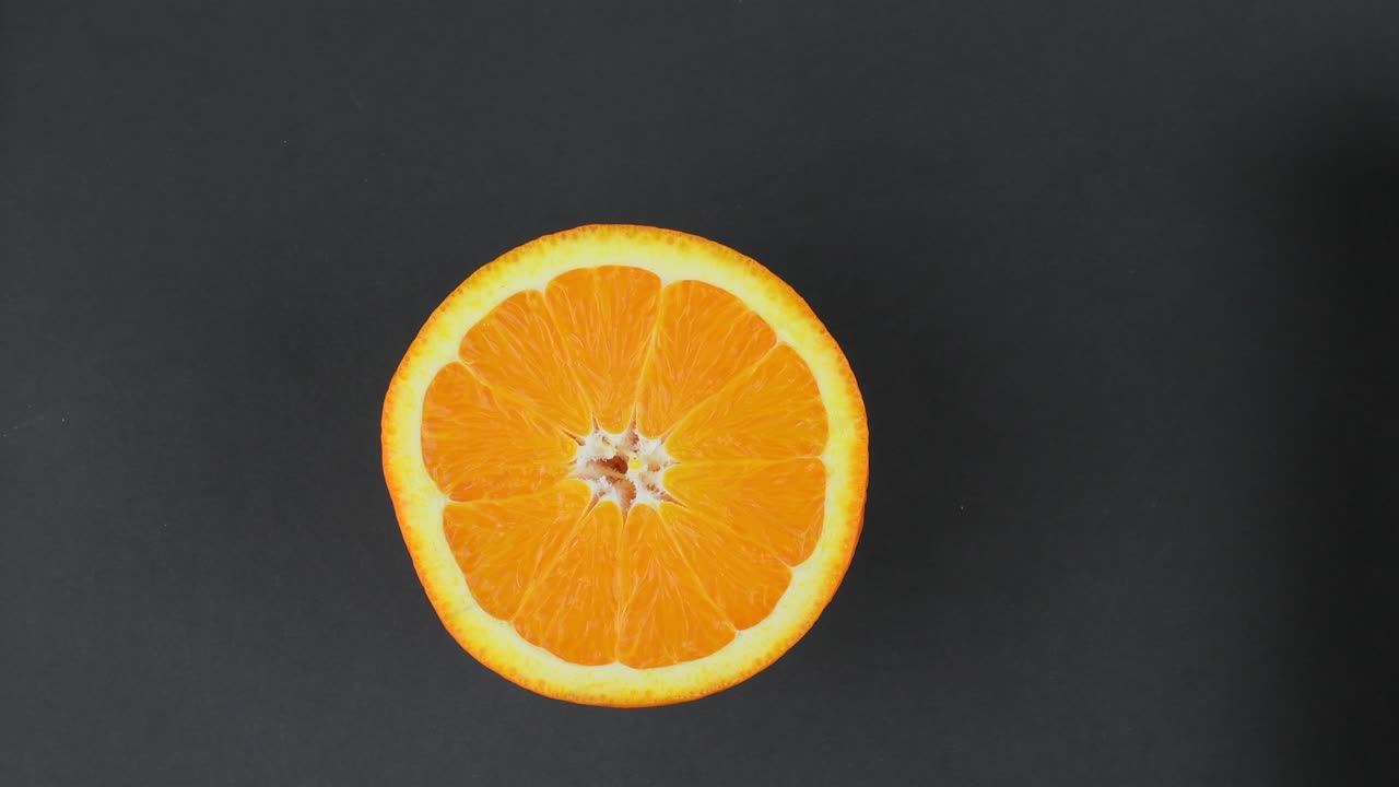 Primo piano di arancia in sezione. Arancia ben illuminata che ruota su sfondo nero. Agrume arancione brillante su sfondo nero. Agrume fresco in loop su sfondo nero. Risoluzione 4K.
