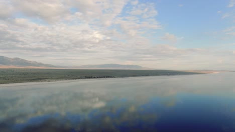lago salado y montañas, llanuras saladas que reflejan el sol, nubes y cielo azul, simetría que refleja el paisaje aéreo movimiento panorámico, tiempo soleado, nubes bonitas, tiro en el mar de salton