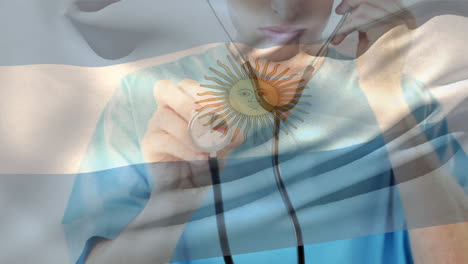 composición digital de la bandera argentina ondeando sobre una trabajadora de salud caucásica con un estetoscopio