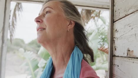 portrait of happy senior caucasian woman relaxing on porch of wooden beach house, in slow motion