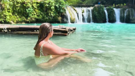 a woman relaxing while sat in the blue waters at cambugahay falls in siquijor, philippines