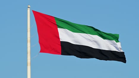 4k 60fps: la bandera de los emiratos árabes unidos ondeando en el aire, el cielo azul de fondo, el símbolo nacional de los emiratos árabes unidos