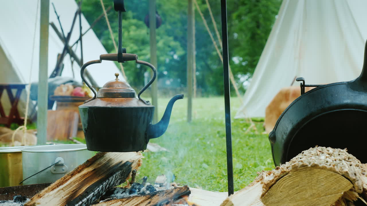 숲의 아메리카 원주민 캠프에서 주전자가 끓고 전경에서 음식이 준비되고 있습니다.