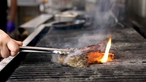 grilling fresh marinated lamb rib chops over the fire, flipping with tongs - close up