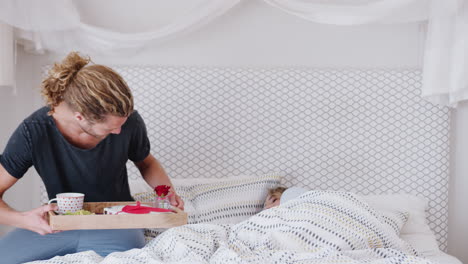 man bringing woman breakfast in bed to celebrate birthday or valentines day