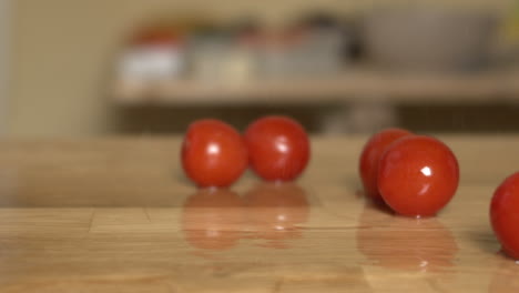 red cherry tomatoes fall on a cutting board with water splashes, apple prores slow-mo camera truck left-right