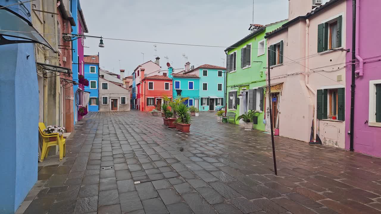 Stendibiancheria con panni stesi attraverso una strada vuota di case dipinte a colori vivaci. Campo lungo.