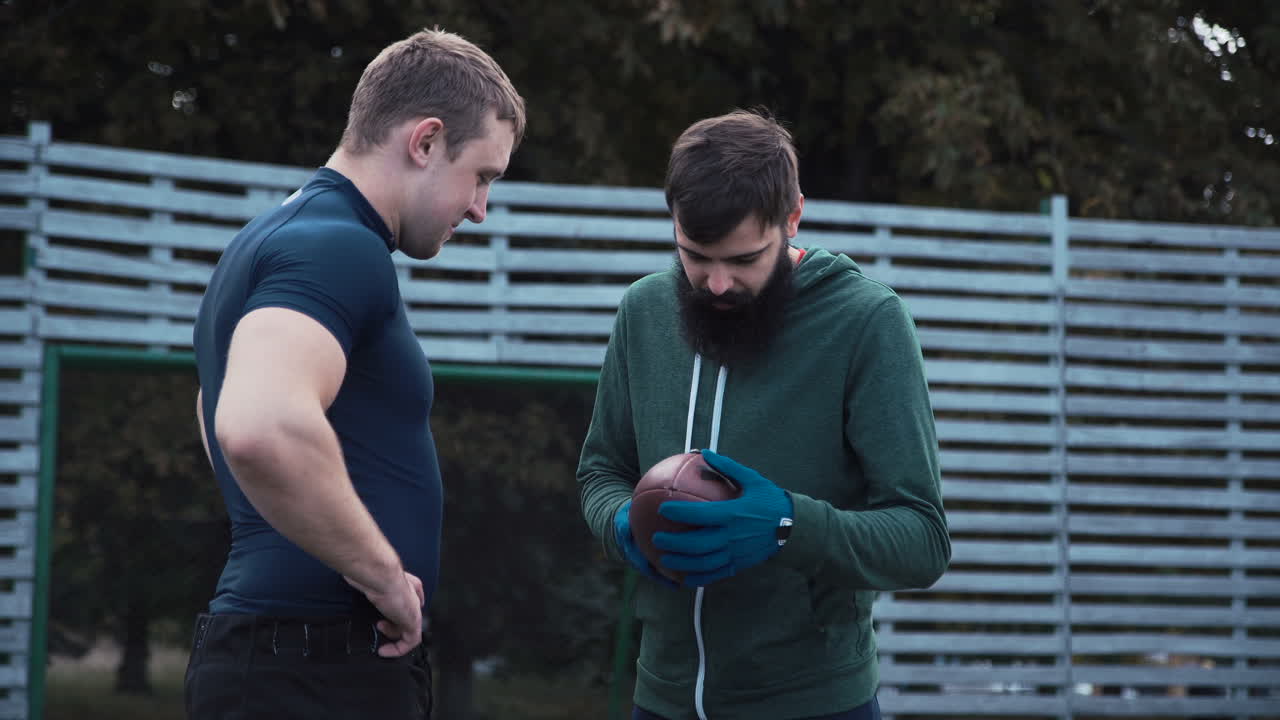 Two men discussing an American football outdoors