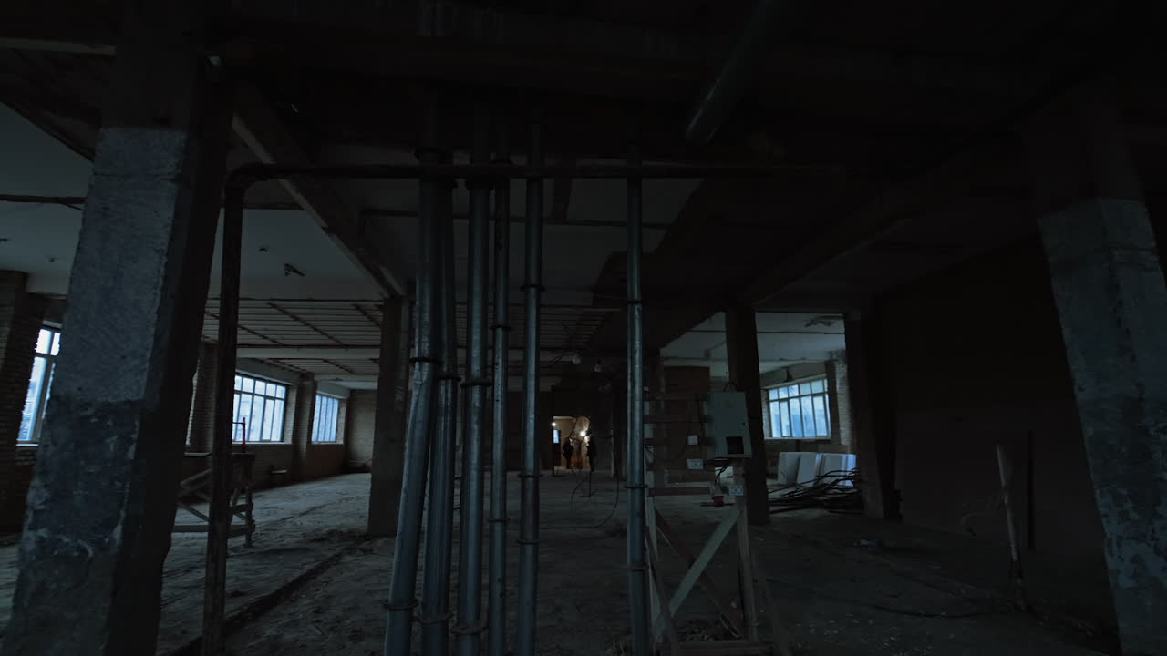 Several metal pipes inside the large room. Interior of the building being constructed. Two builders at backdrop.