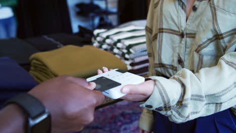 Man-In-Clothing-Store-Making-Contactless-Payment-At-Sales-Desk-Holding-Credit-Card-To-Reader