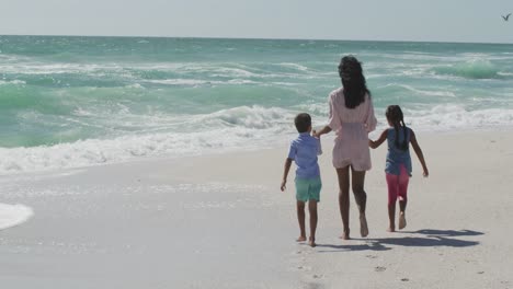 back view of hispanic mother with daughter and son walking on beach
