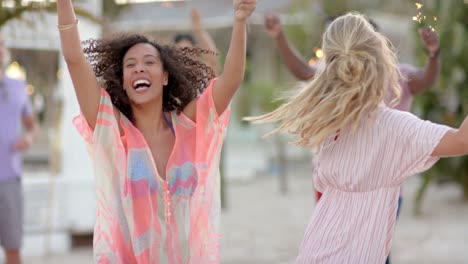 happy diverse group of friends dancing with sparklers at beach