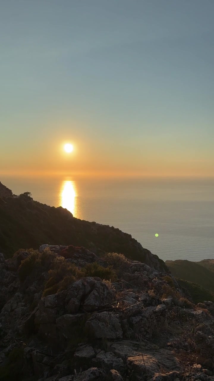 Um pôr do sol deslumbrante brilha sobre o mar e as falésias rochosas em Buggerru, Sardenha, Itália - Foto vertical.