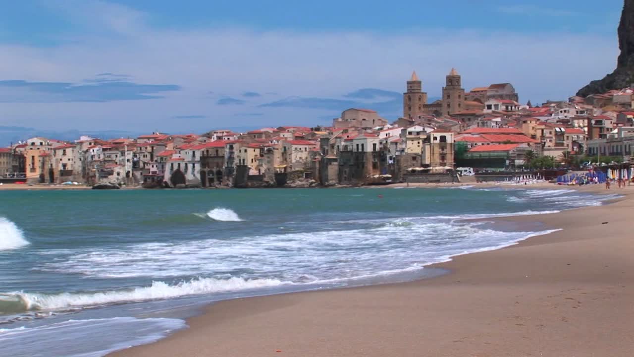 Piccole onde si infrangono vicino a case lungo una costa a Cefalù, Italia.
