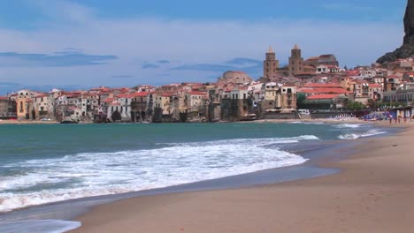 Small-waves-break-near-houses-along-a-shoreline-in-Cefalu-Italy--