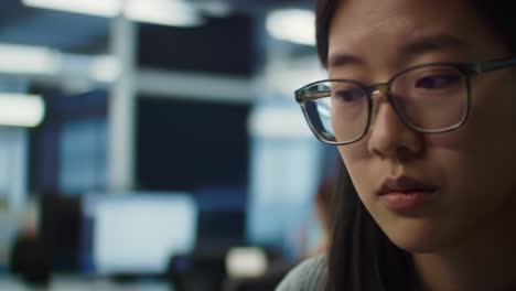 focused female professional in glasses contemplates her work in a modern office environment, showcasing intensity and concentration amidst technology