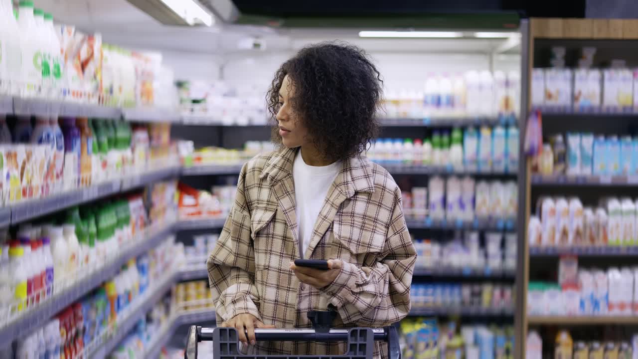 African American lady checking grocery list on smartphone at supermarket
