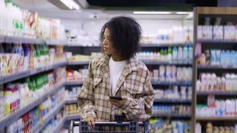 african american lady checking grocery list on smartphone at supermarket