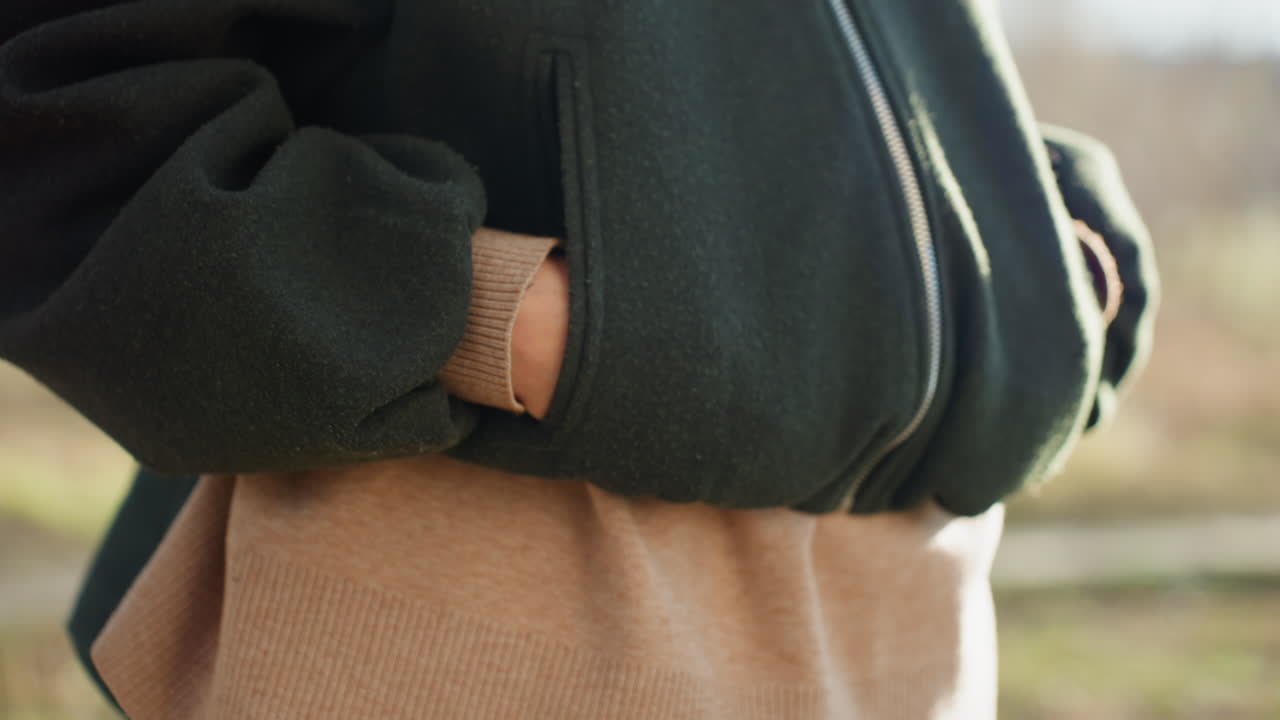 Close up view of dark green wool jacket with visible metal zipper worn over beige sweater outdoors in daylight showing casual winter fashion detail texture fabric style warmth clothing