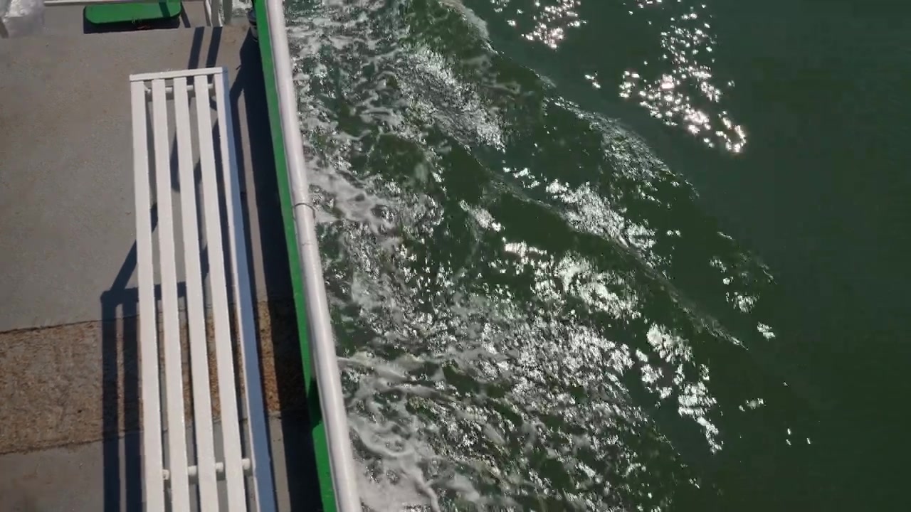 Ha Long Bucht, Quảng Ninh, Vietnam. Eine Ansicht von einem fahrenden Boot fängt glitzerndes Buchtwasser und das Deck des Schiffes bei hellem Tageslicht ein. Handgehalten.