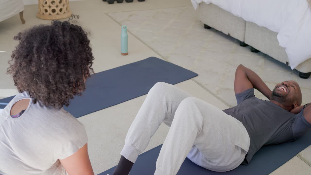 Couple in sportswear on blue mats, woman holding shoes starting man doing situps for abs