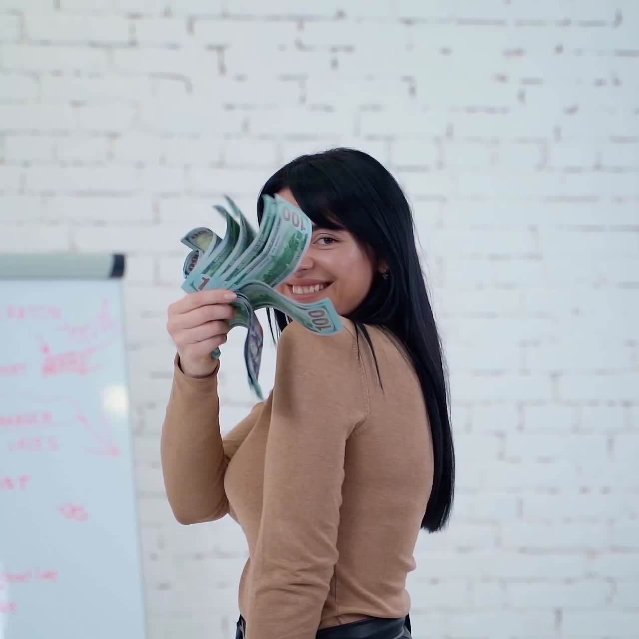 Portrait of smiling woman with dollar banknotes. Satisfied business woman holding a big amount of money and is waving cash in office.