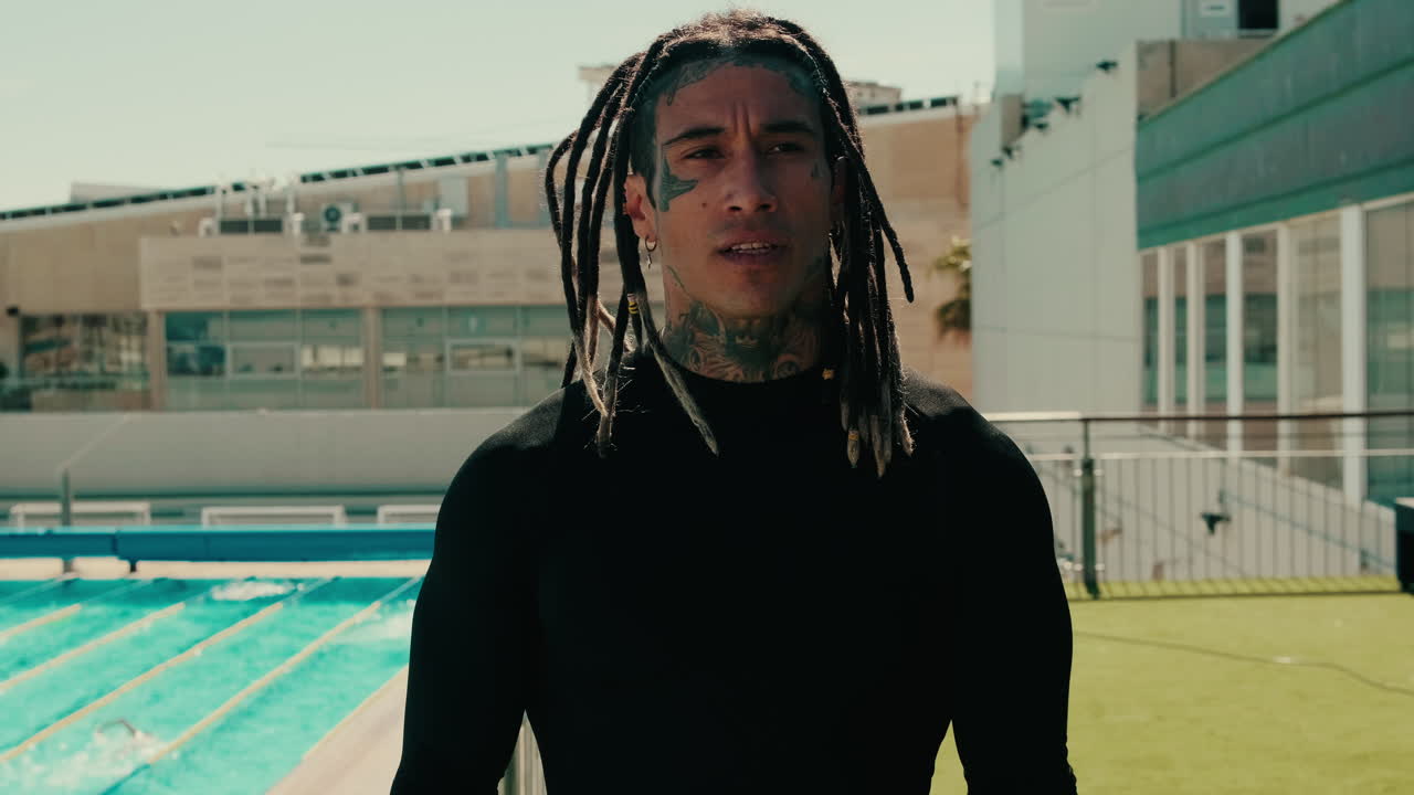 Uomo pensieroso con dreadlocks e tatuaggi che osserva l'oceano.
