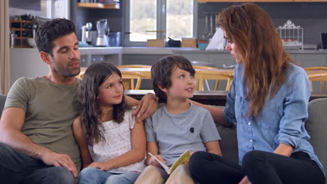 family sit on sofa in lounge talking and reading book together