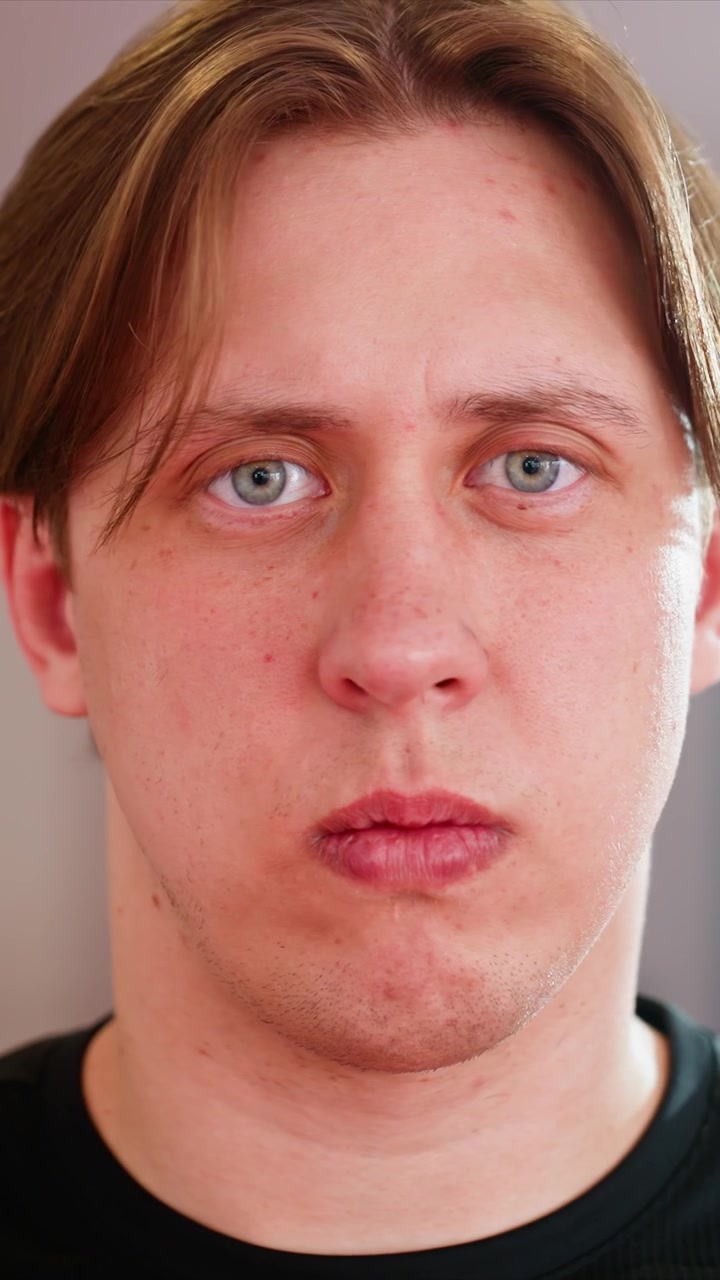 Zbliżenia profilowe młodego mężczyzny z jasnobrązowymi włosami. Mężczyzna poprawia postawę szyi, unosząc ręce. W tle wyściełany sprzęt i rozmyte okrągłe światła