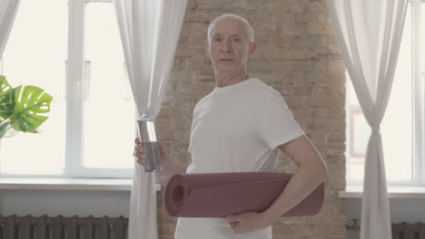 viejo macho posando con una estera de yoga y mirando a la cámara