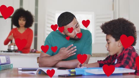 Animation-of-social-media-heart-icons-over-smiling-biracial-man-and-son-doing-homework