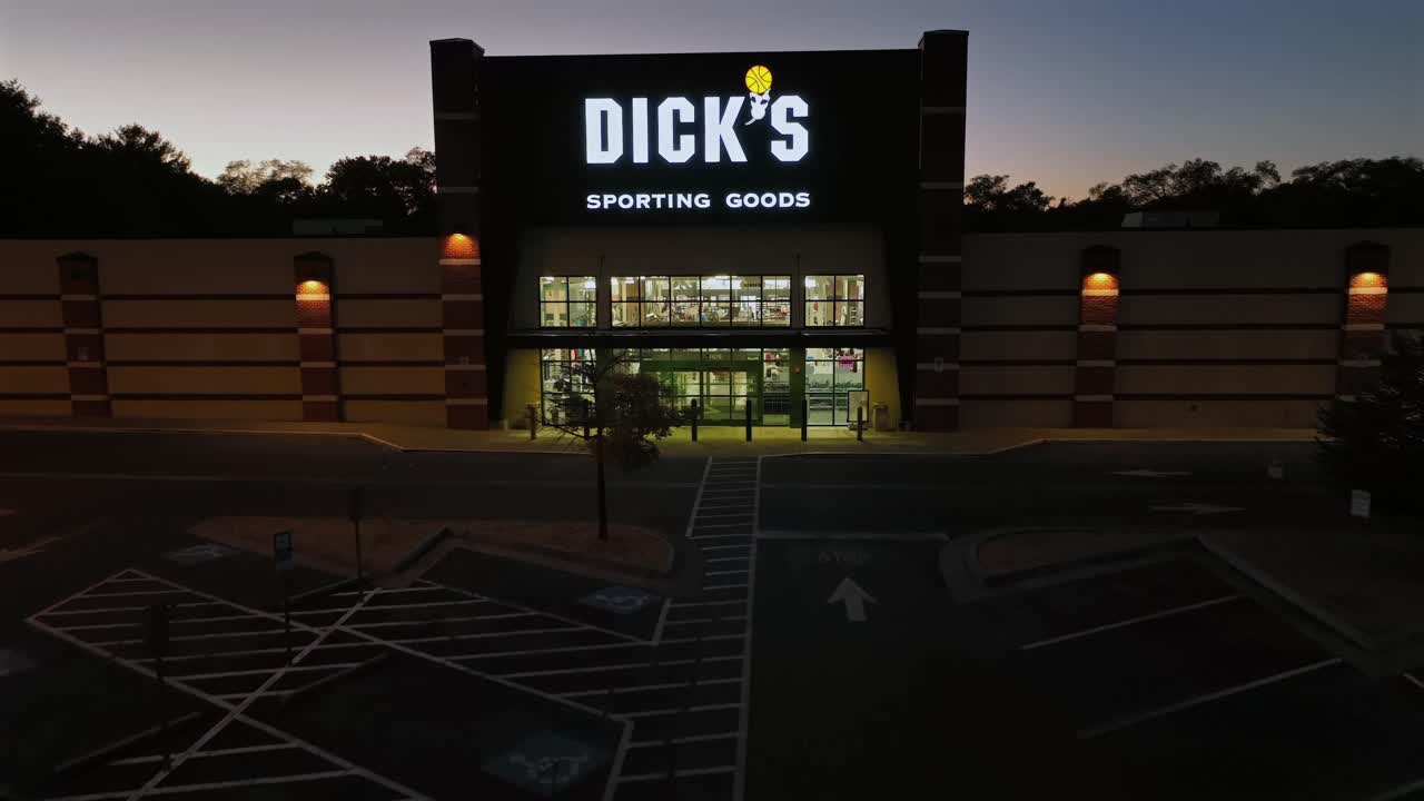 Aerial approaching shot of Dick´s Sporting Goods Storefront at dusk. Empty parking area with lighting entrance doors. Wide shot