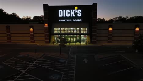 aerial approaching shot of dick´s sporting goods storefront at dusk. empty parking area with lighting entrance doors. wide shot