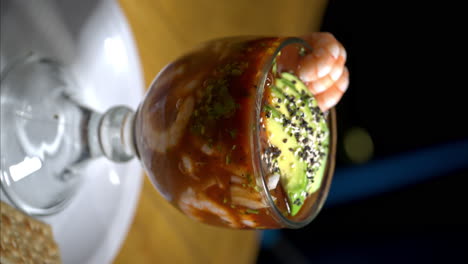 cerrado vertical de un cóctel de camarón de mariscos servido en una taza de vidrio con aguacate y algunos camarones en la parte superior