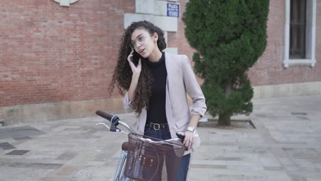 young woman on bicycle talking on phone in city
