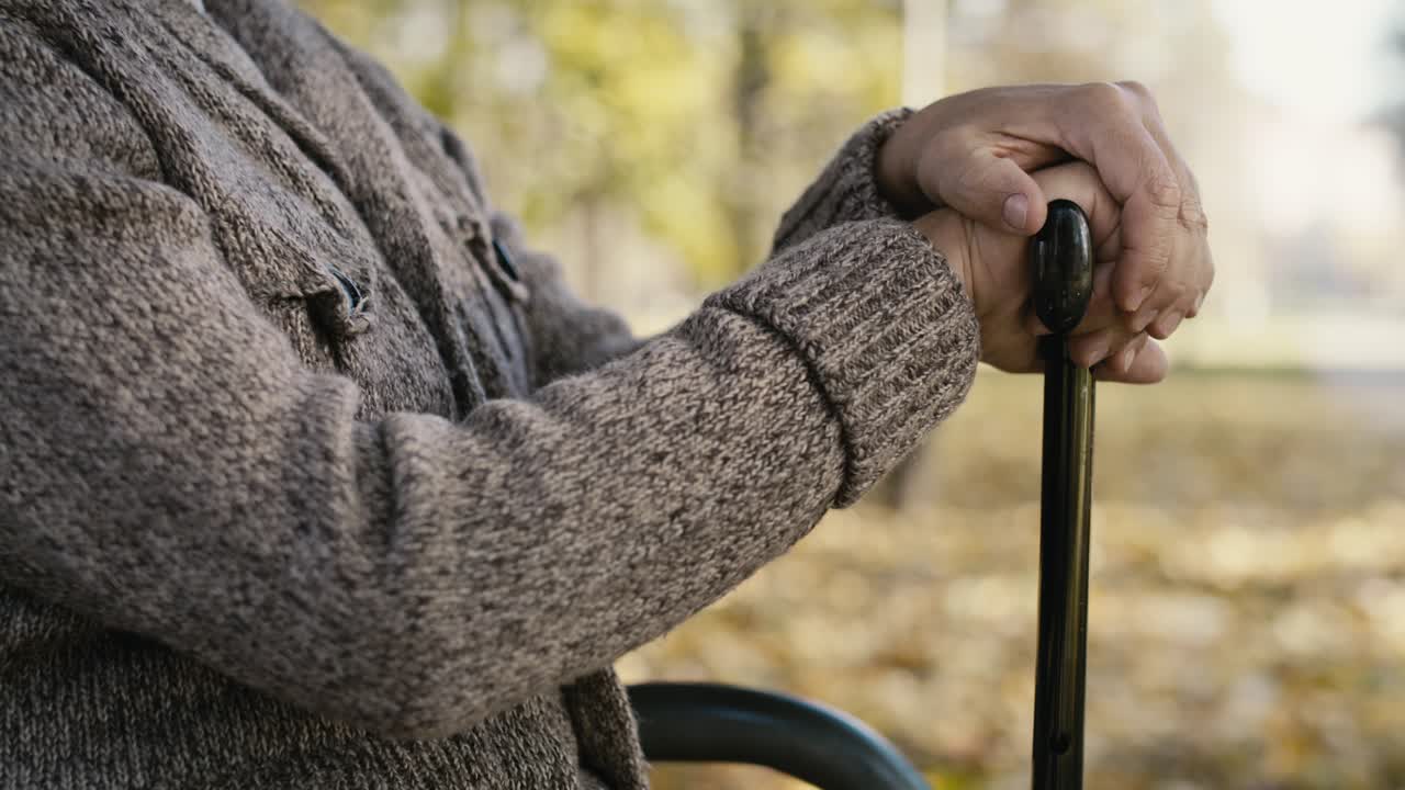 Close up of old caucasian man with hands on walking stick sitting on bench in park