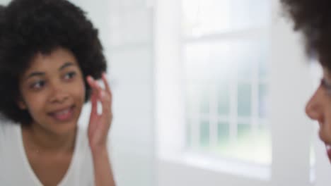 African-american-woman-touching-her-face-while-looking-in-the-mirror-at-bathroom