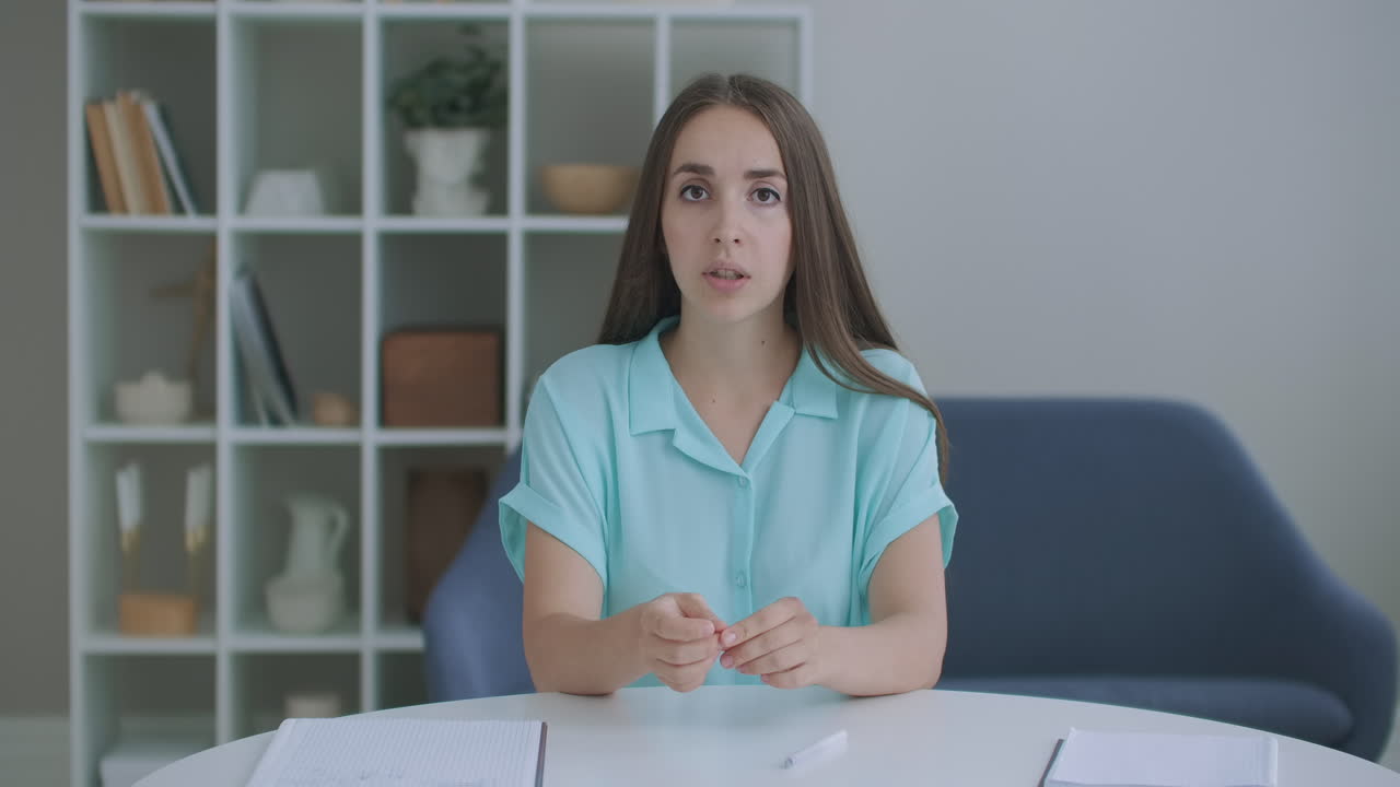 Head shot woman sit on couch look at camera greeting friend start video call. Young adult female with short curly hairstyle enjoy pleasant conversation by video conference event concept