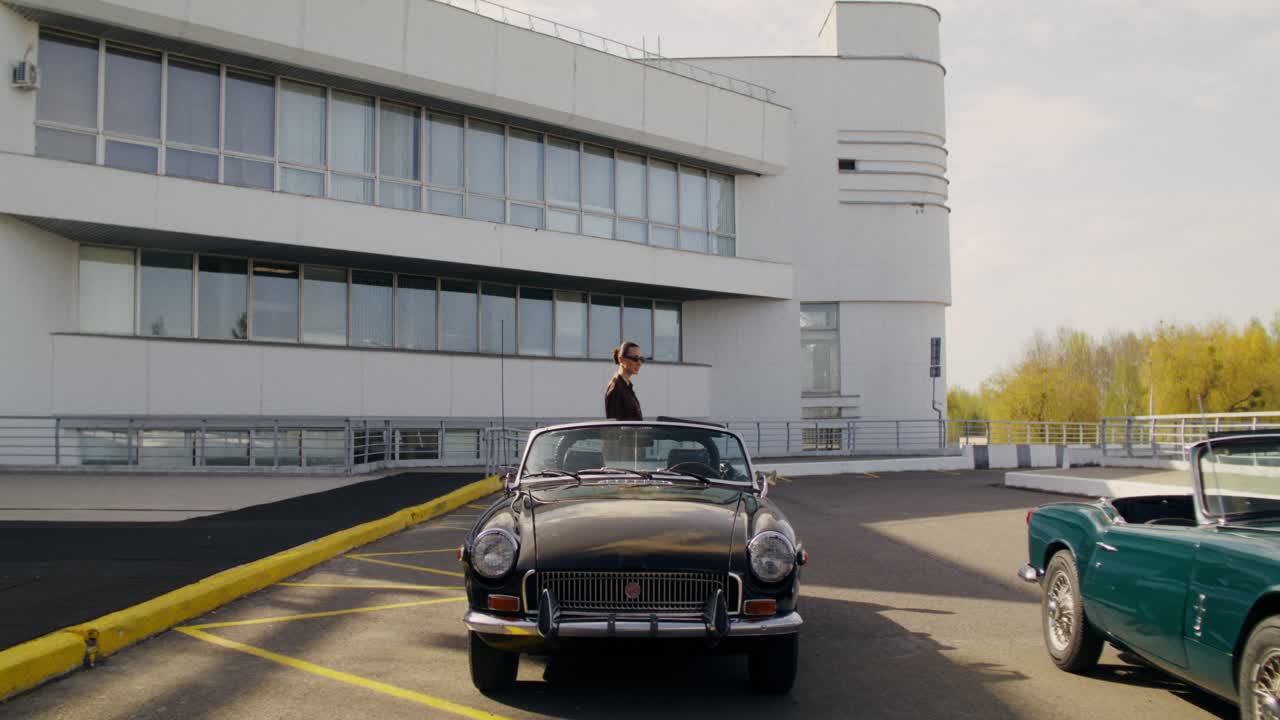 Woman standing near a vintage car in front of a modern building