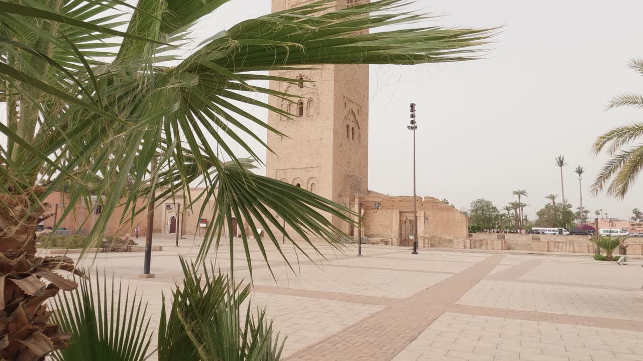 establecimiento de la vista de la torre de la mezquita de koutoubia desde detrás de las hojas de palmeras ornamentadas soplando en la brisa