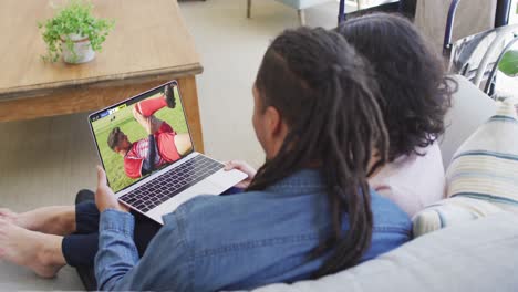 video de una pareja afroamericana sentada en el sofá y viendo fútbol en la computadora portátil en casa