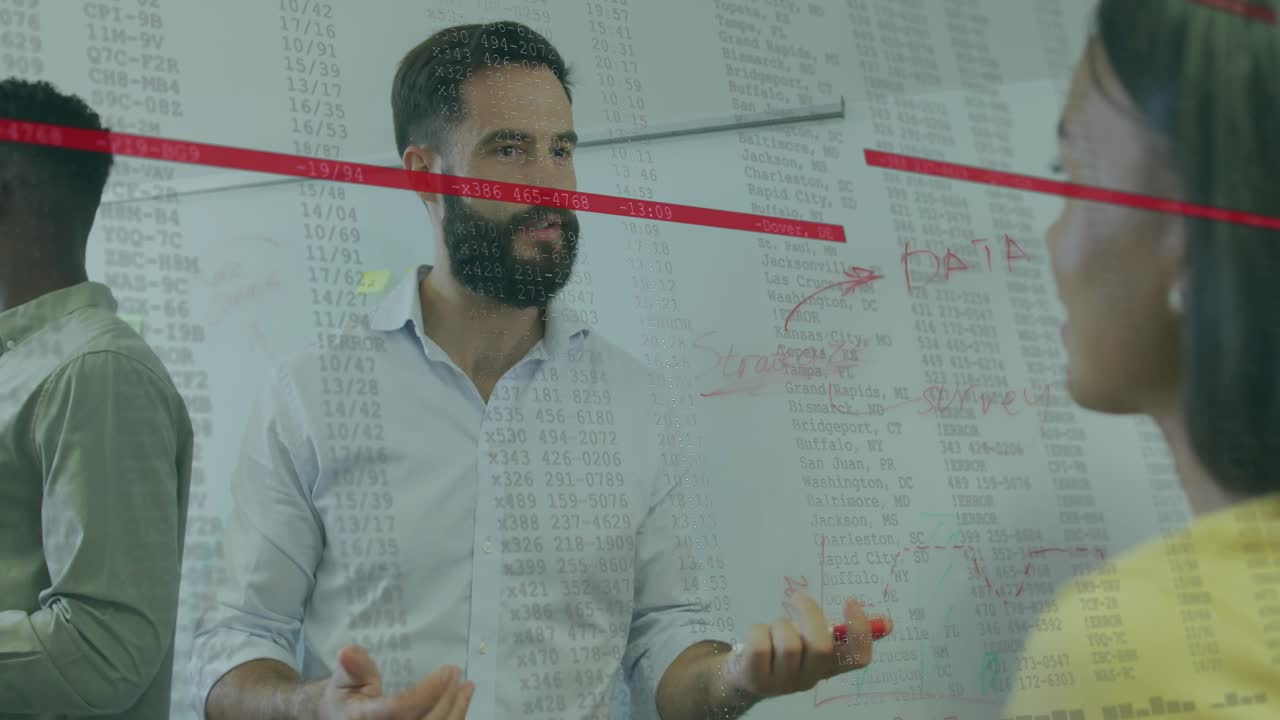 Bearded presenter tapping marker on glass board explaining business data as colleague raises hand