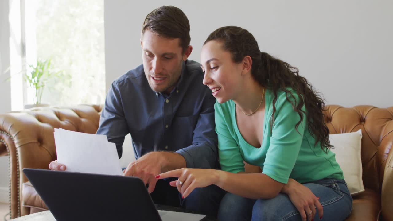 Una pareja caucásica joven hablando y pagando sus facturas usando una computadora portátil