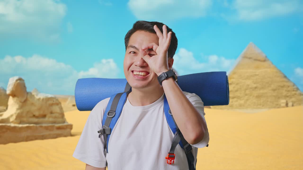 Close Up Of Asian Male Hiker With Mountaineering Backpack Smiling And Showing Ok Sign With Fingers Over Eyes While Traveling In Pyramid Of Giza
